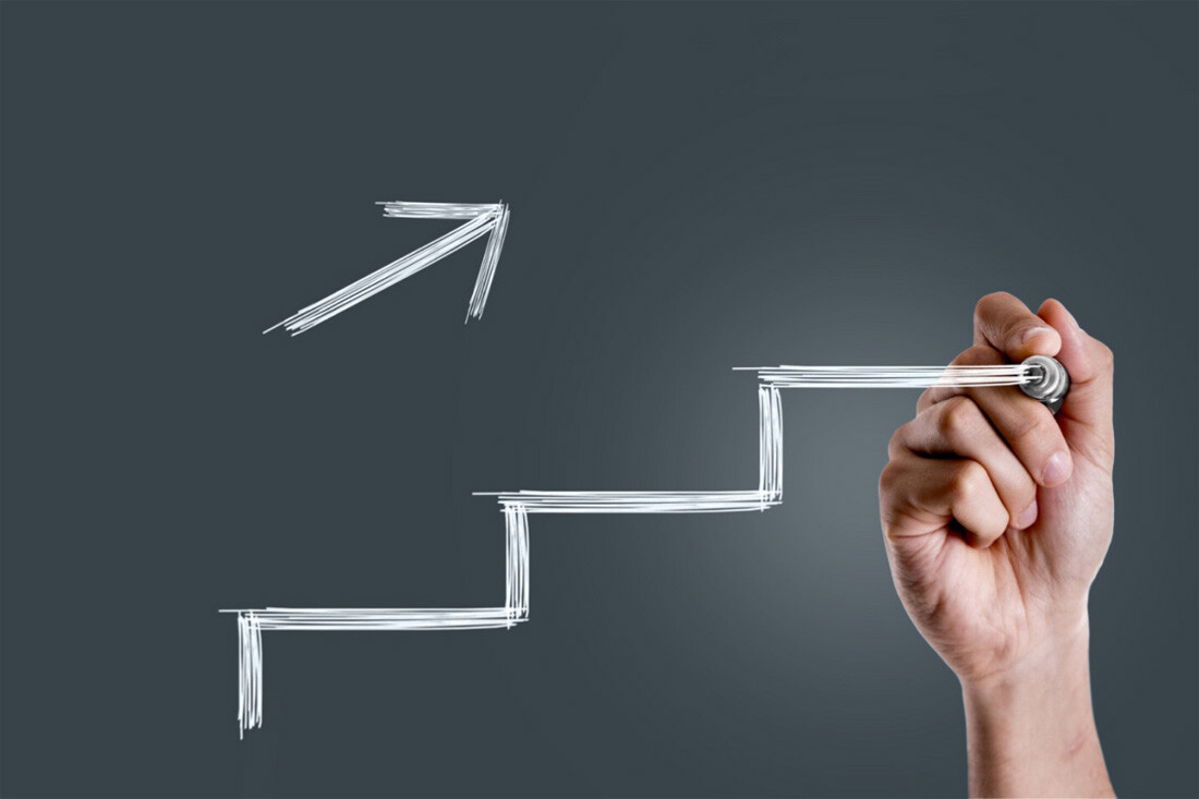 An employee drawing on a whiteboard - stairs and an arrow pointing up and to the right to signal stepping up work productivity.