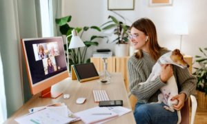 A woman working from home for a hybrid company on a zoom call with her dog.