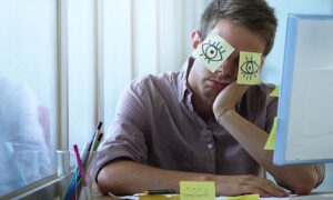 An employee sleeping at his desk with post-it notes over his eyes, making anyone wonder how to prevent quiet quitting.