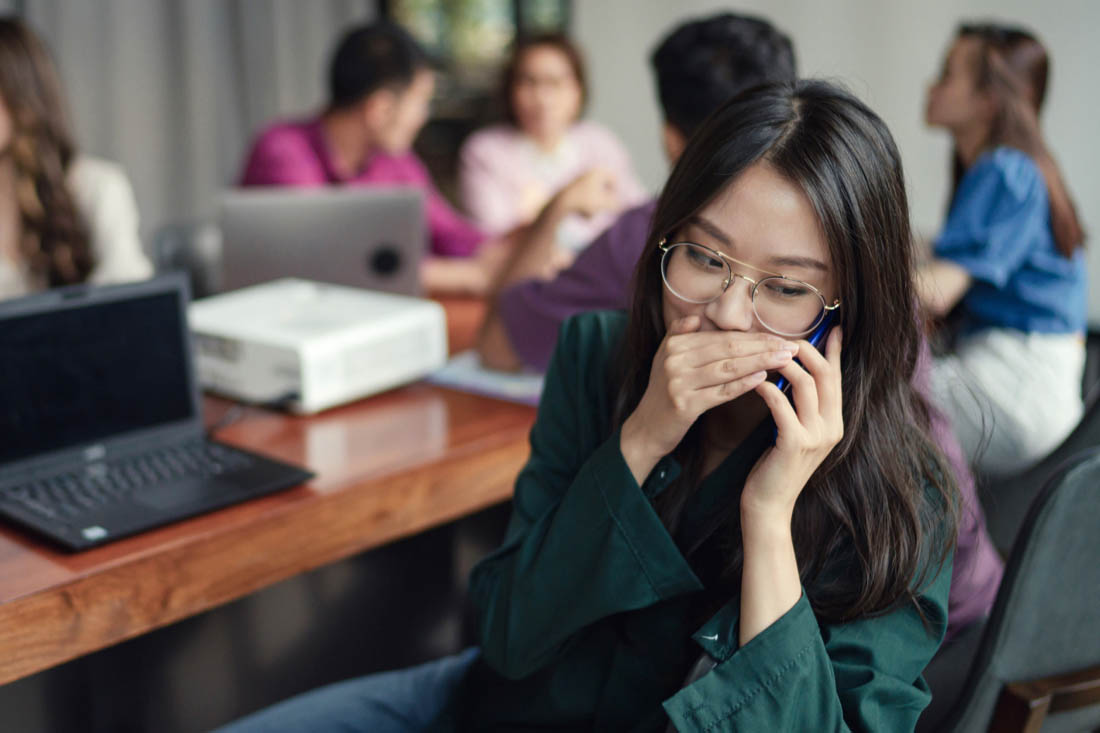 Woman whispering on a phone after being disrupted in a workplace meeting