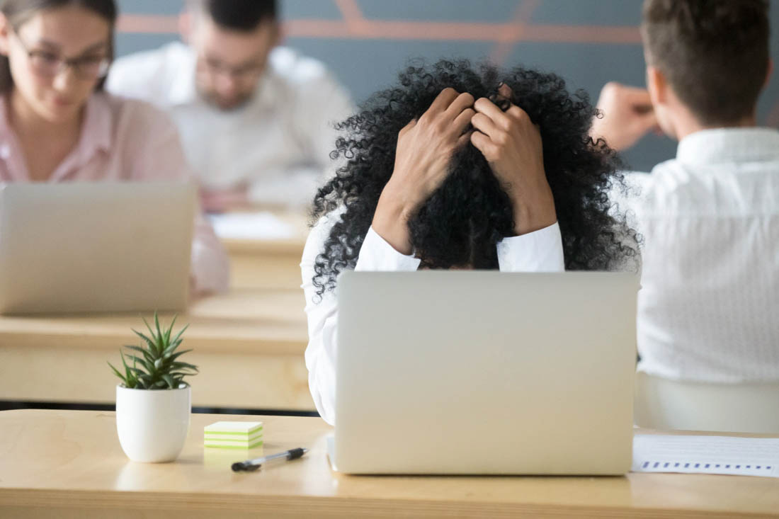 An overwhelmed employee at their desk with their head in their hands.