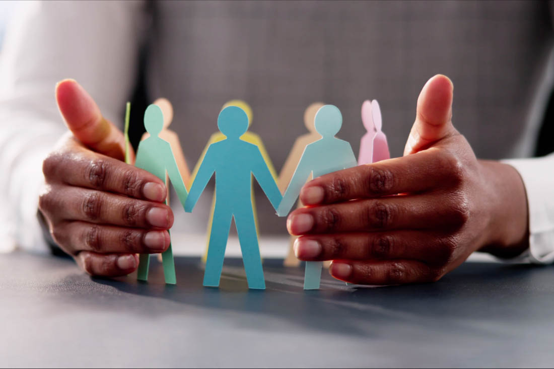 A person with their hands around a circle of paper cutouts or people to symbolize supporting employees in the workplace