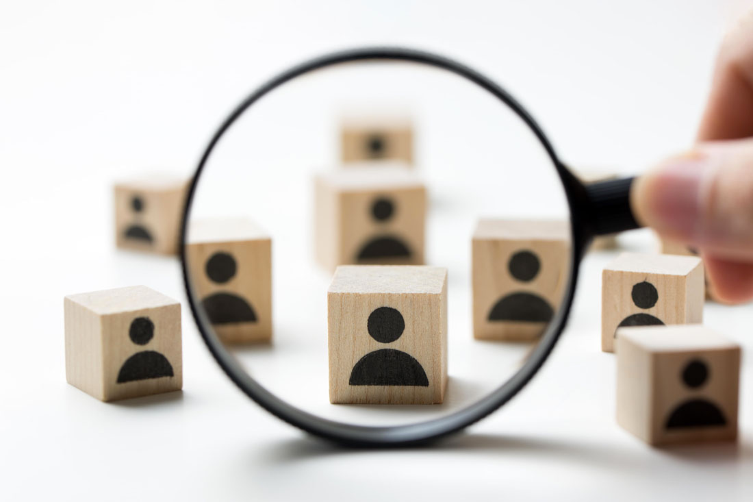 Wooden blocks with employee icons and a magnifying glass highlighting one block to signify talent analytics.