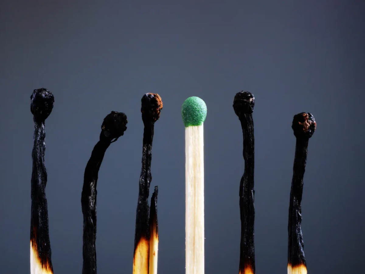 One unlit match with a green tip in the middle of a line of five burned-out matches.