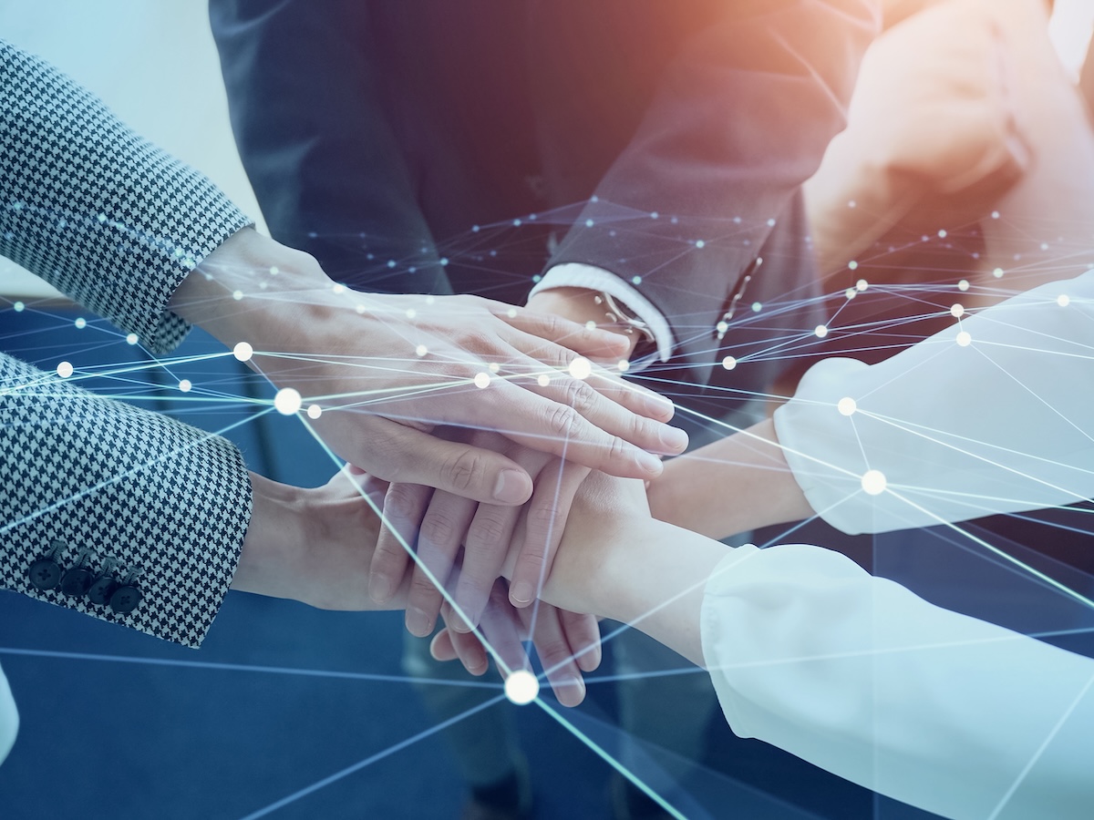 Diverse business team members stack hands in teamwork, overlaid with glowing digital network lines symbolizing collaboration and unity.