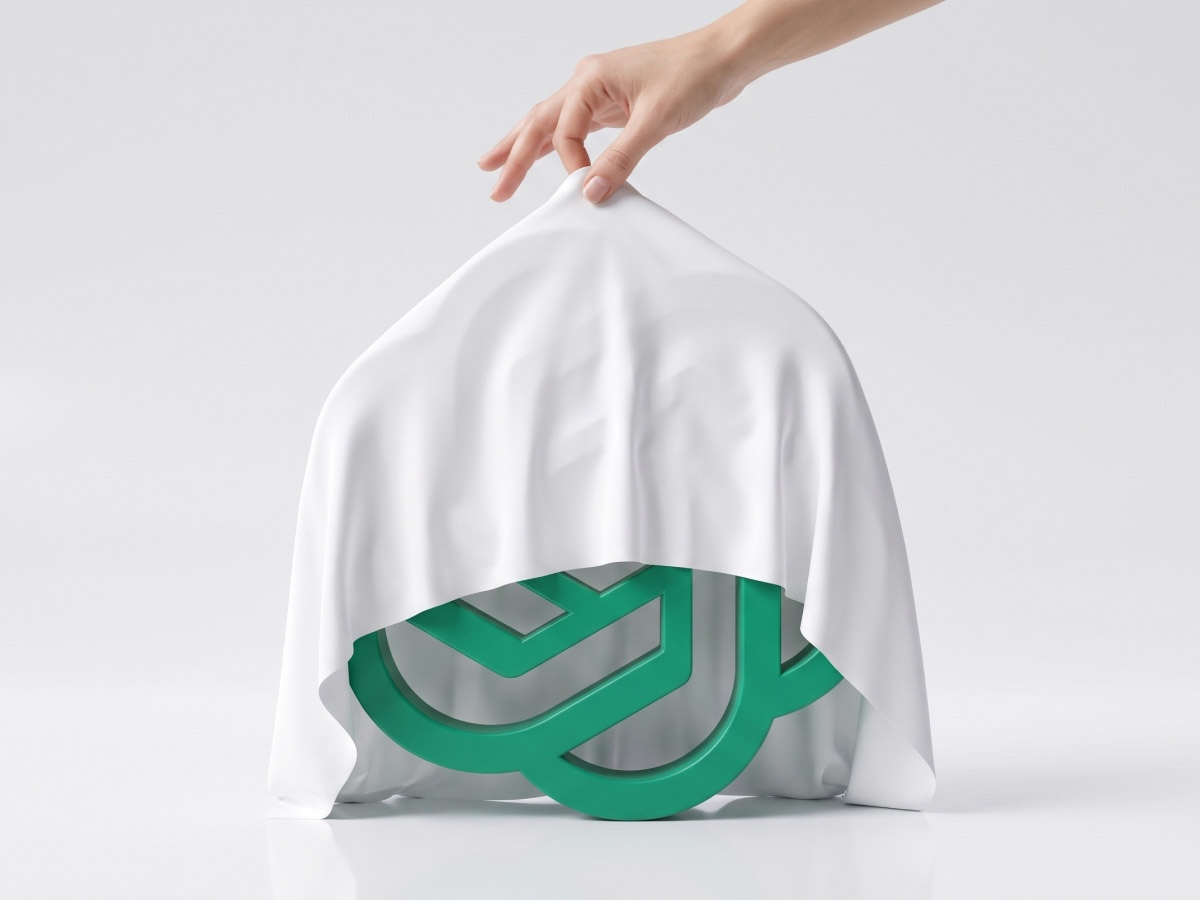 A hand lifting a white sheet to partially reveal a green geometric logo beneath on a clean white background.